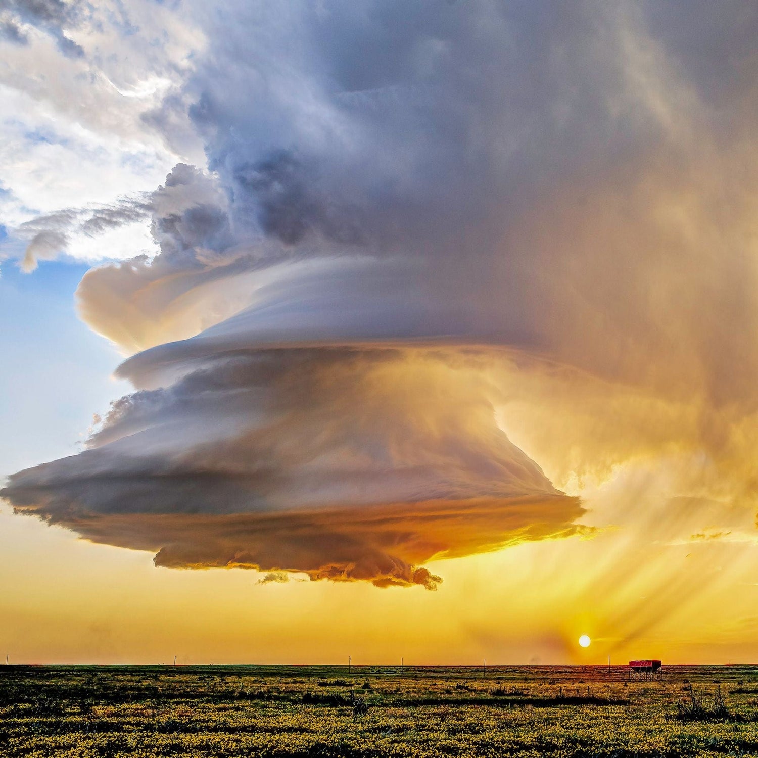 Dramatic cloud formation over a flat landscape during sunset with a truck visible on the horizon.
