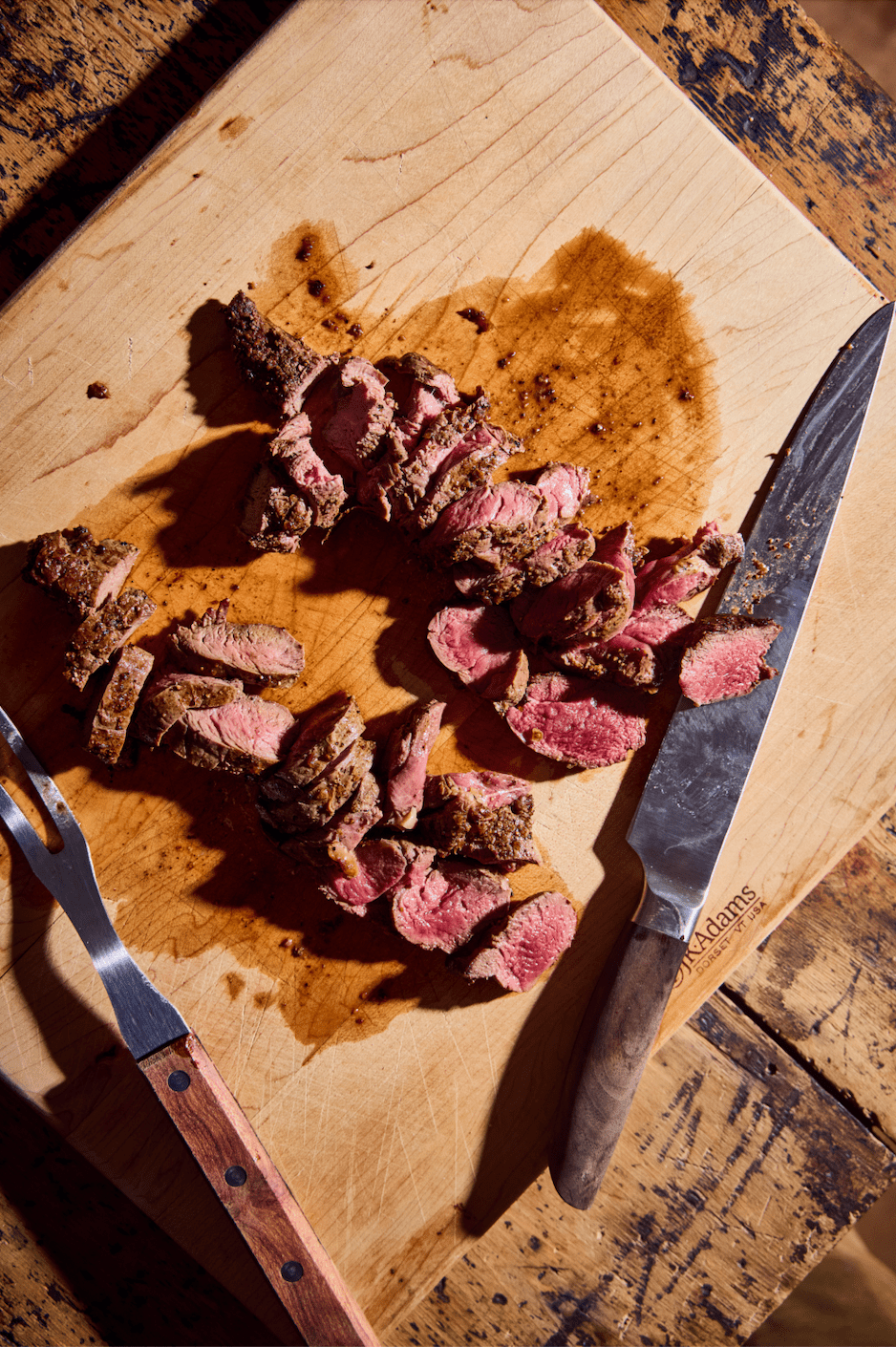 Sliced cooked beef on a wooden cutting board, with a knife and fork placed beside it.