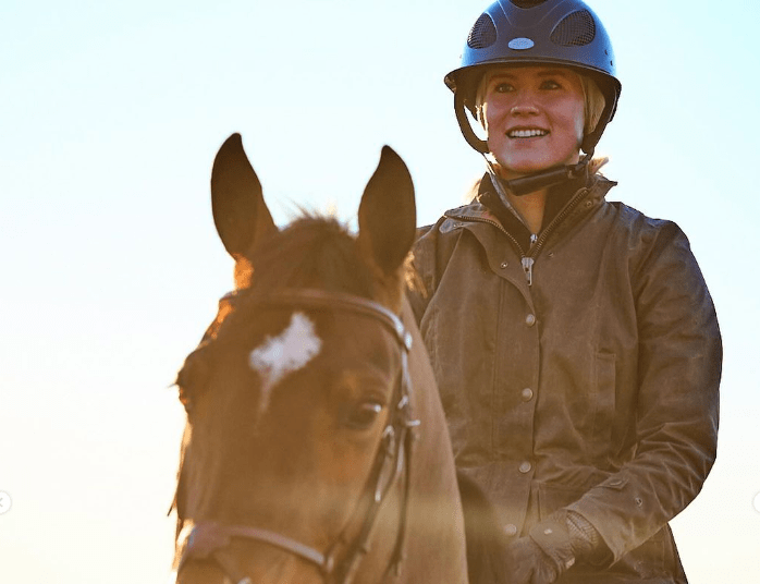 Person wearing a helmet and jacket, riding a horse outdoors with a clear sky in the background.