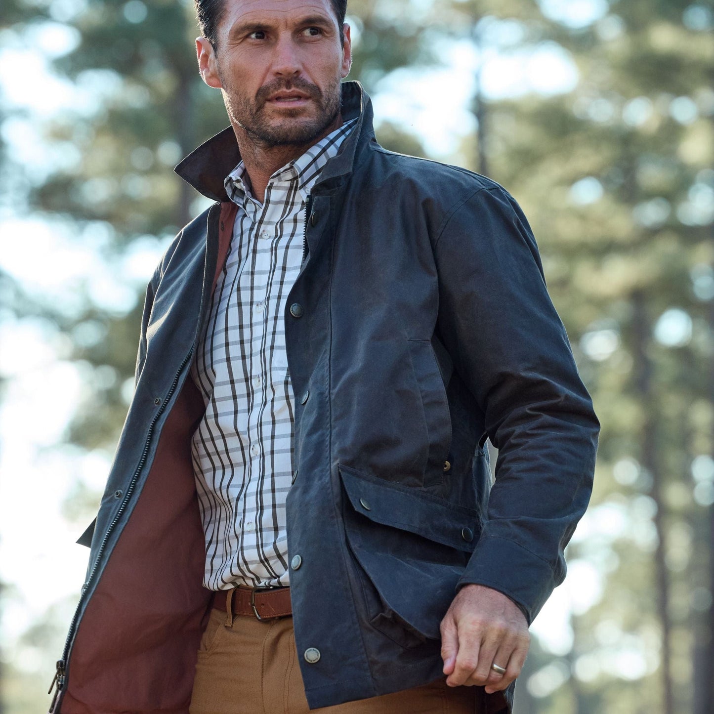 Man in a classic fit dark jacket and Tom Beckbes Monroe Poplin Shirt stands outdoors, trees in the background.