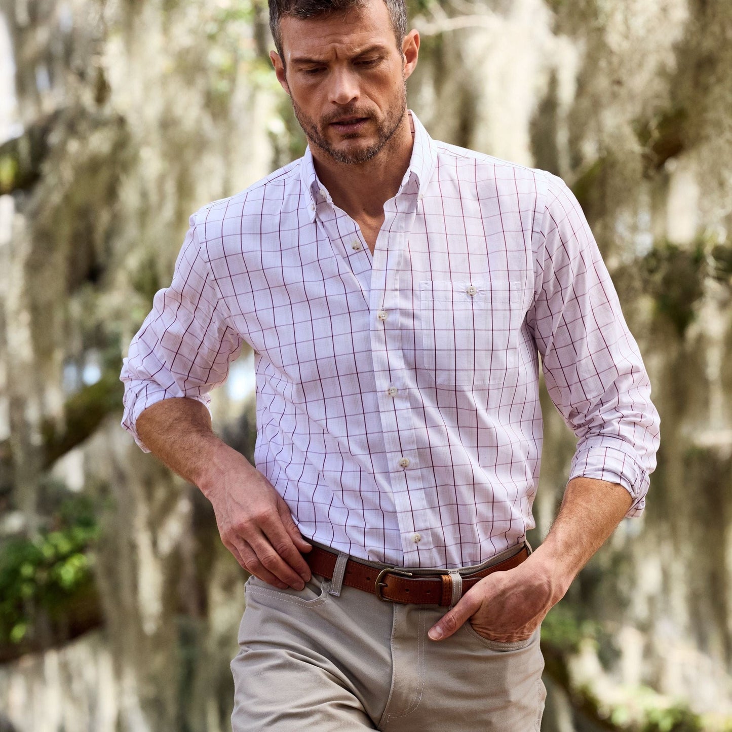 Man in a Monroe Poplin Shirt and beige pants walks outdoors with blurred trees in the background, Tom Beckbe style.