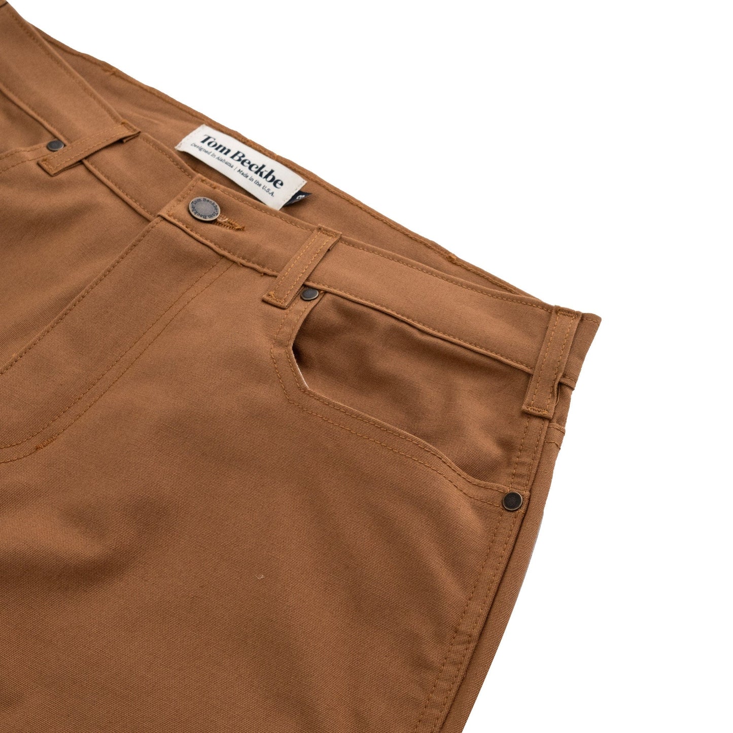 The Redmont Pant by Tom Beckbe is made from durable cotton, with front pockets and a visible waistband label.