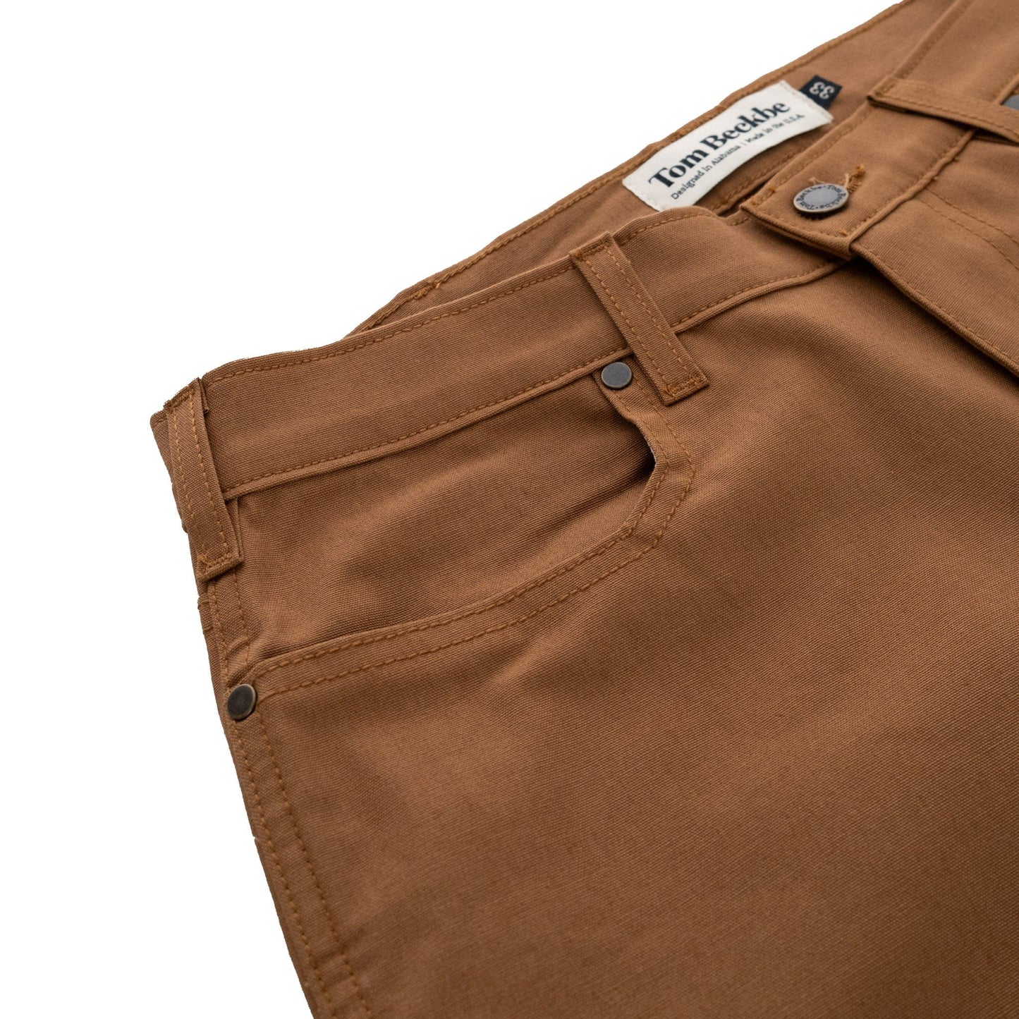 The Redmont Pant by Tom Beckbe features durable cotton, visible stitching, black rivets, and a branded waistband label.