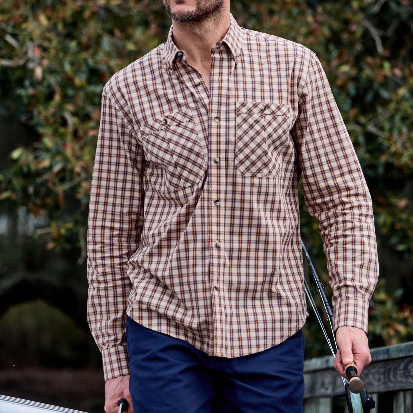 A man in a Tom Beckbe Tidewater Shirt with UPF 30+ holds rods while walking outdoors.
