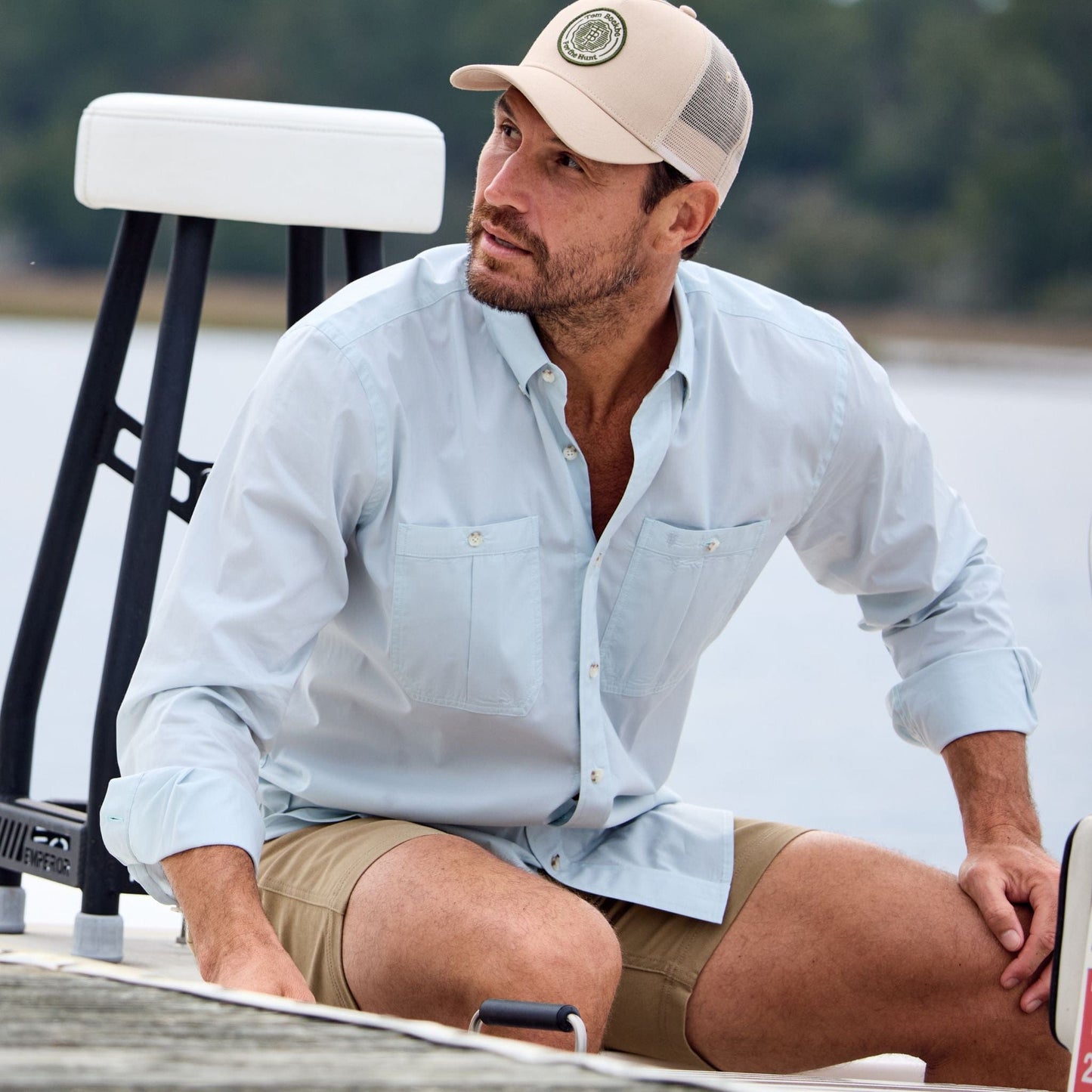 Man on a boat in Tom Beckbe’s Tidewater Shirt with UPF 30+ coverage, light blue shorts, and a beige cap looking sideways.