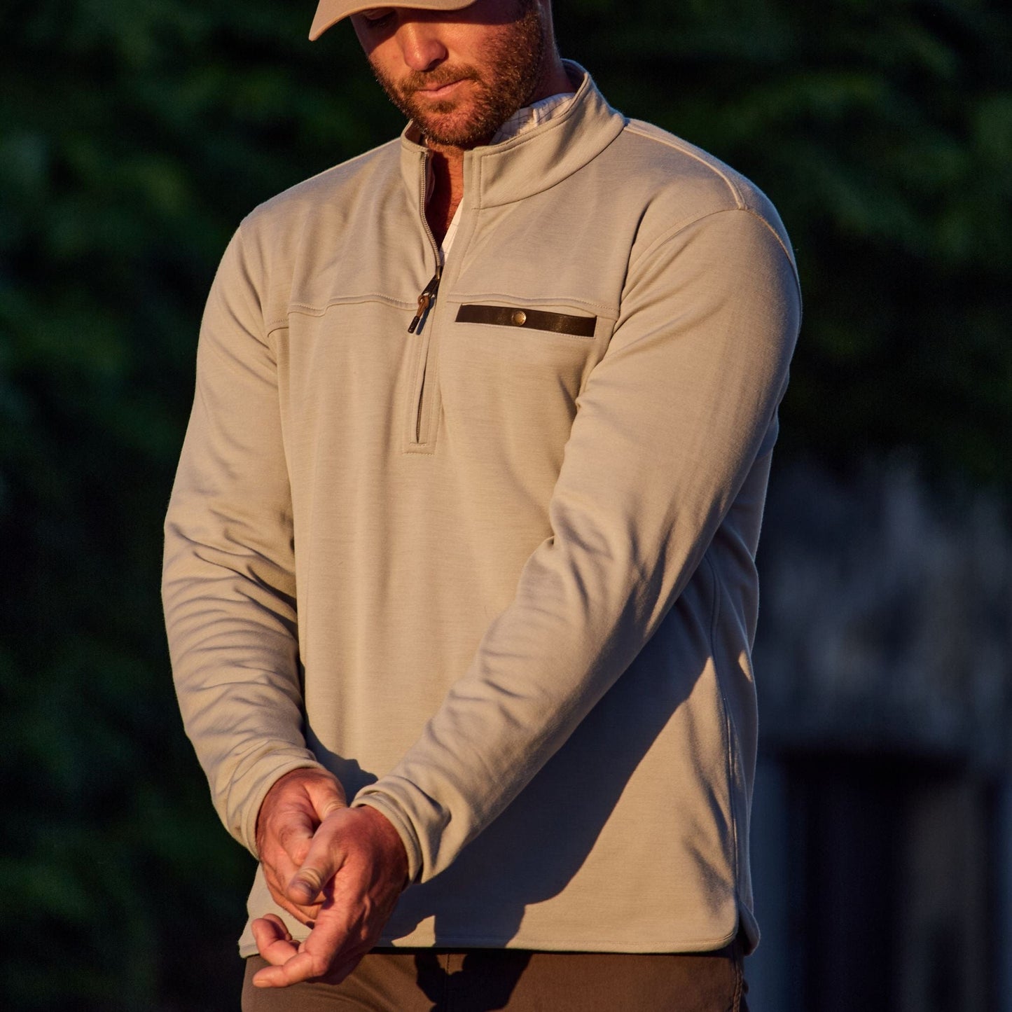 A person adjusts the sleeve of their beige Tom Beckbe Tucker Fleece Quarter Zip outdoors.