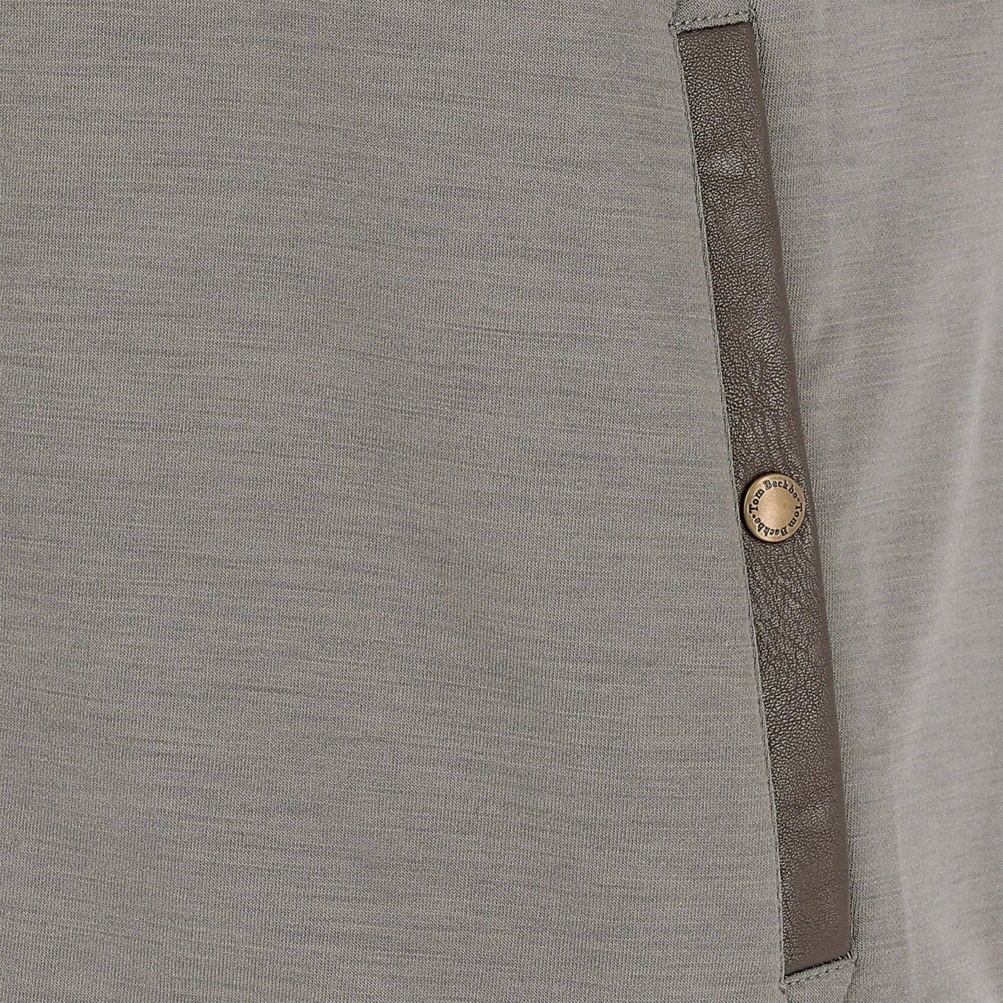 Close-up of a gray fabric garment with a brown vertical trim and a single round metallic button.