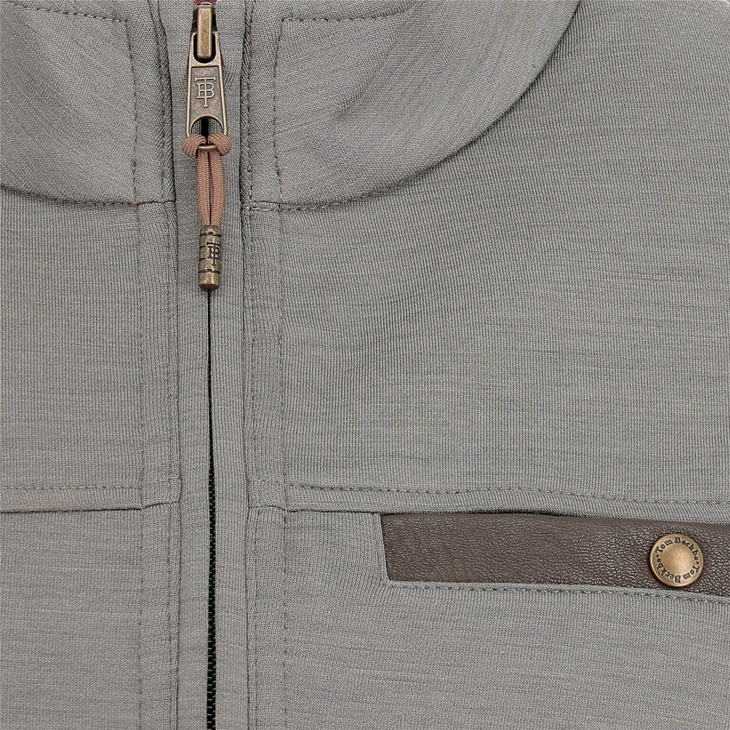 Close-up of a light grey zip-up jacket with a brown horizontal pocket trim and a metallic button detail.