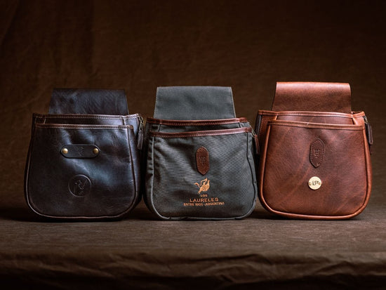 Three leather pouches in black, green, and brown are displayed side by side against a dark fabric background.