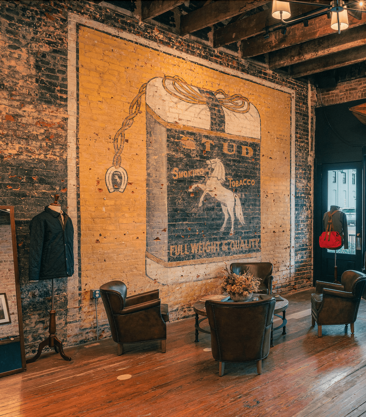 Wall with a vintage tobacco advertisement featuring a horse, surrounded by classic furnishings and a suit on a mannequin.