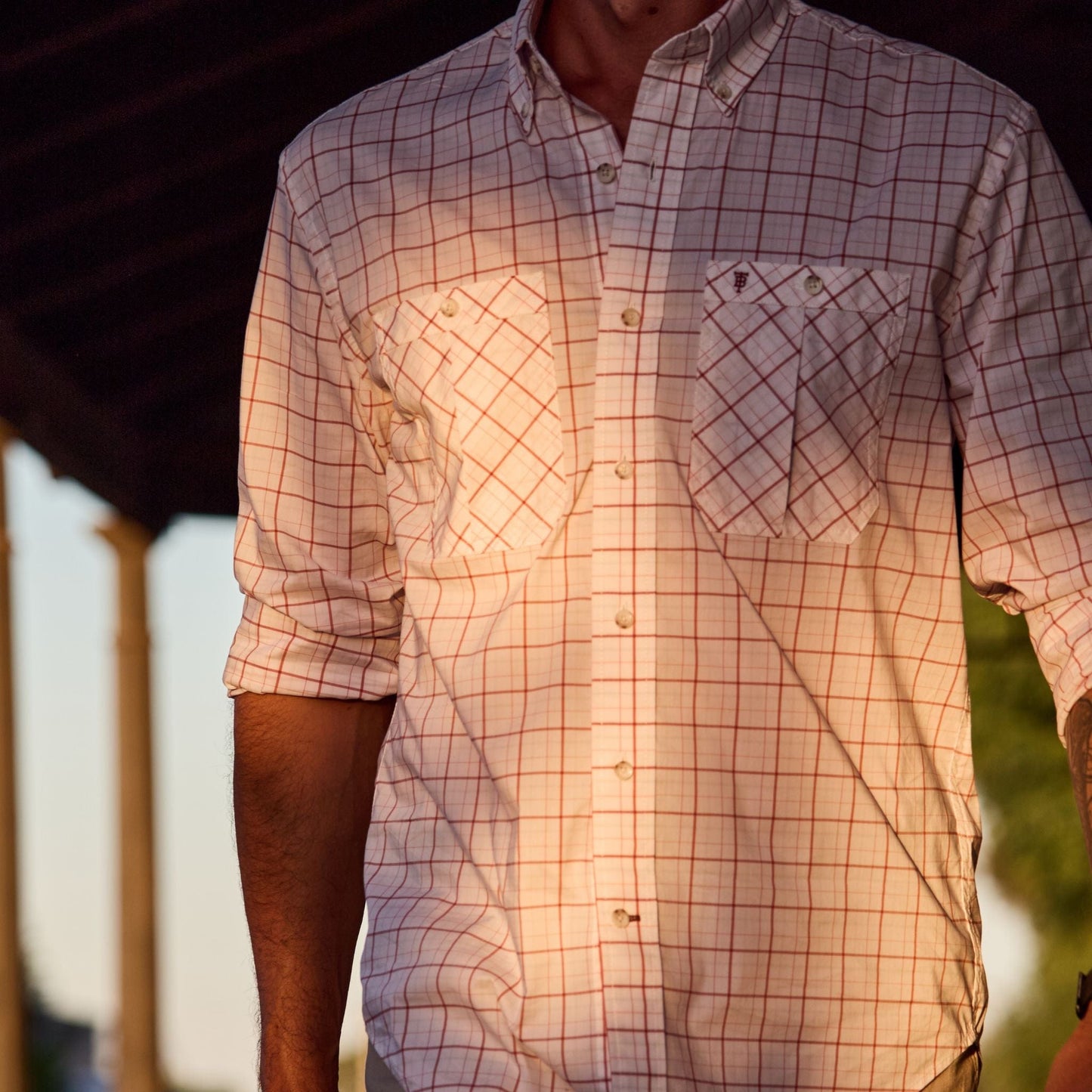 A person in a plaid Tidewater Shirt by Tom Beckbe explores outdoors, enjoying UPF 30+ coverage as sunlight casts shadows.