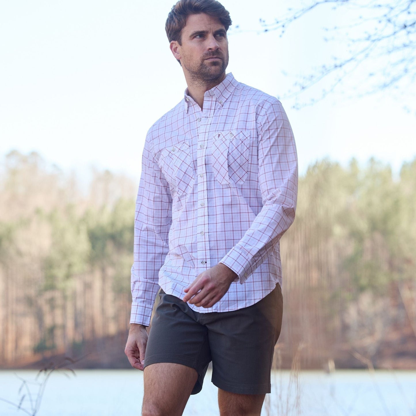Man in a Tom Beckbe Tidewater Shirt and dark shorts walking near a wooded area.