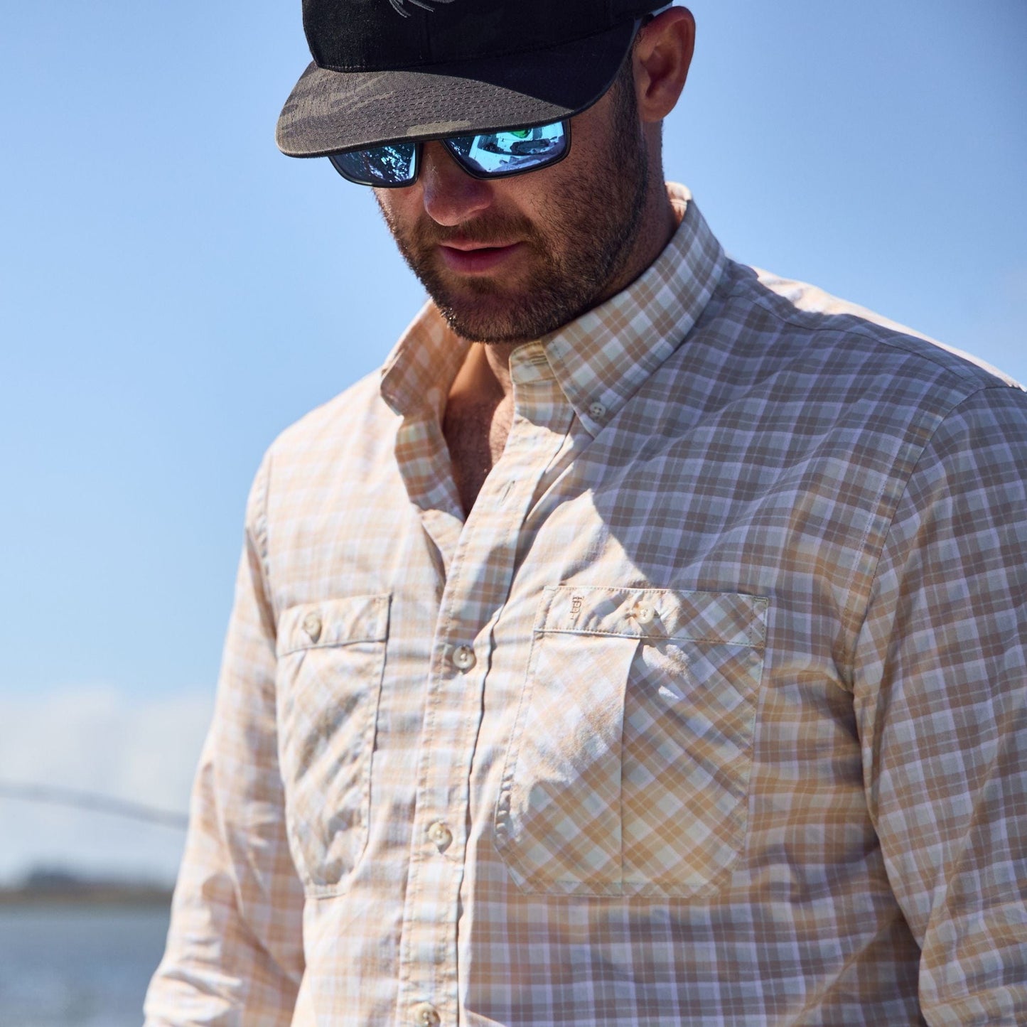 Man in sunglasses and a Tom Beckbe Tidewater Shirt stands under a clear blue sky.