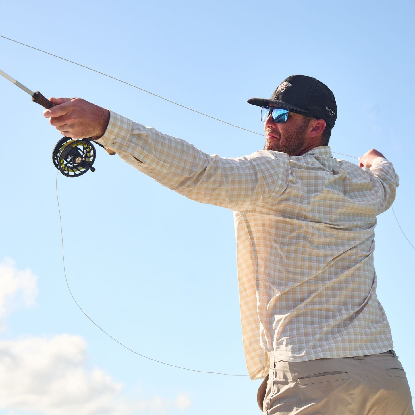 A man casts a fly rod in a Tom Beckbe Tidewater long sleeve for UPF 30+ protection, wearing sunglasses and a cap.
