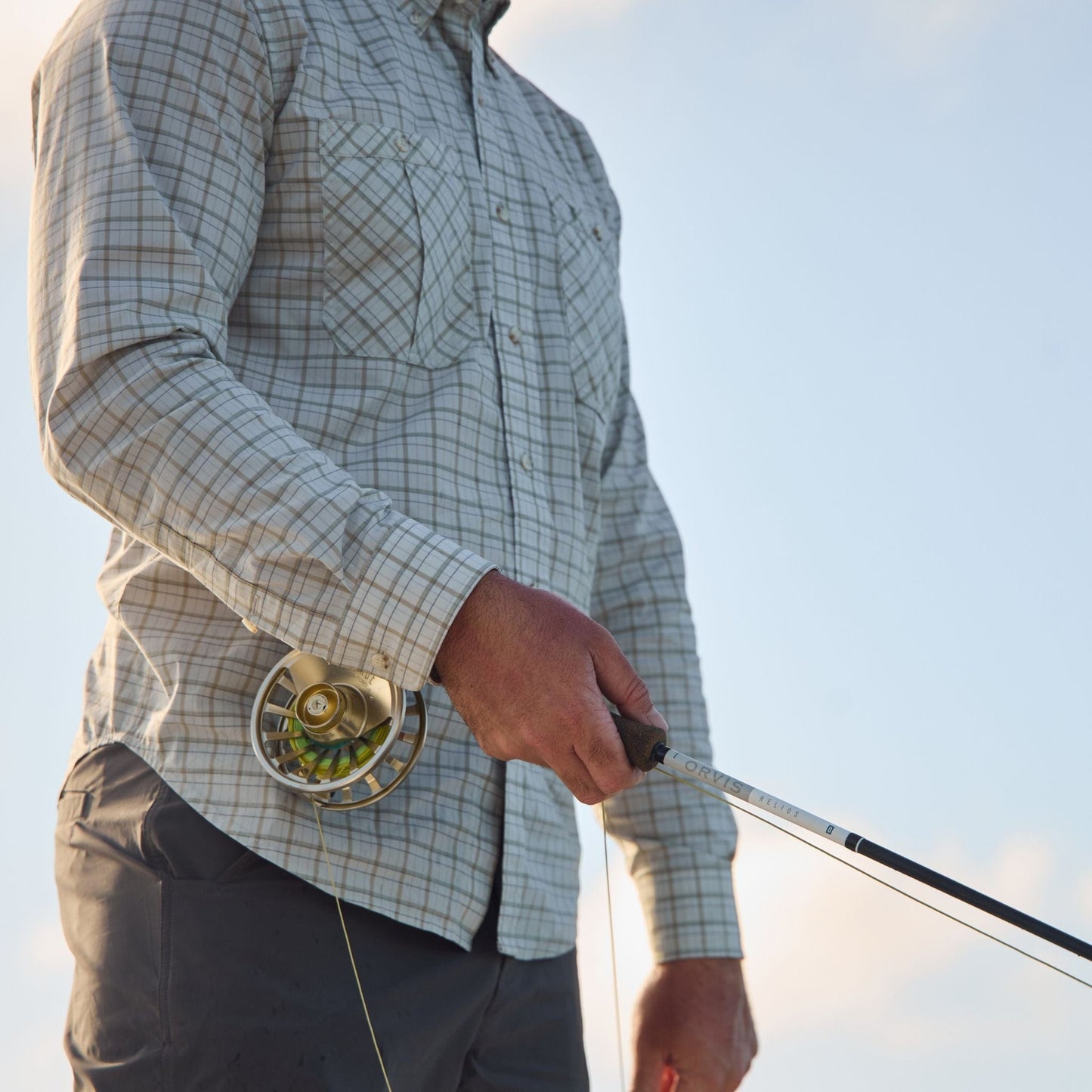 Someone in a Tom Beckbe Tidewater Shirt holds a rod, enjoying the clear sky.
