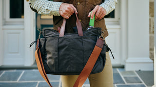 A person pours liquid from a metal flask with a leather case into a small metal cup.