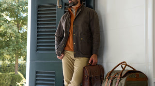 A person wearing a light shirt carries a two-tone canvas and leather messenger bag with buckled straps over their shoulder.