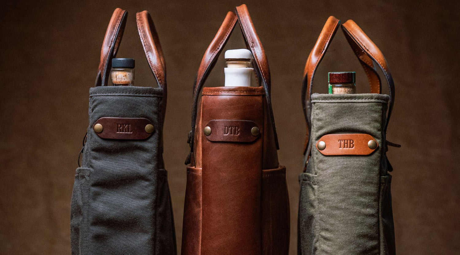 Three wine tote bags, each containing a bottle and featuring leather handles and personalized leather tags with initials: RKM, DTB, and THB.