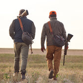 Two people in outdoor clothing carrying Tom Beckbe Canvas Blind Bags and rifles, ready for waterfowl adventures.