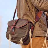 Person with a Tom Beckbe Canvas Blind Bag and brown jacket in an outdoor setting.