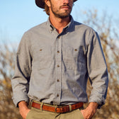 Man wearing a Tom Beckbe Dixon Brushed Cotton Twill Shirt, brown belt, and hat outdoors with trees in the background.