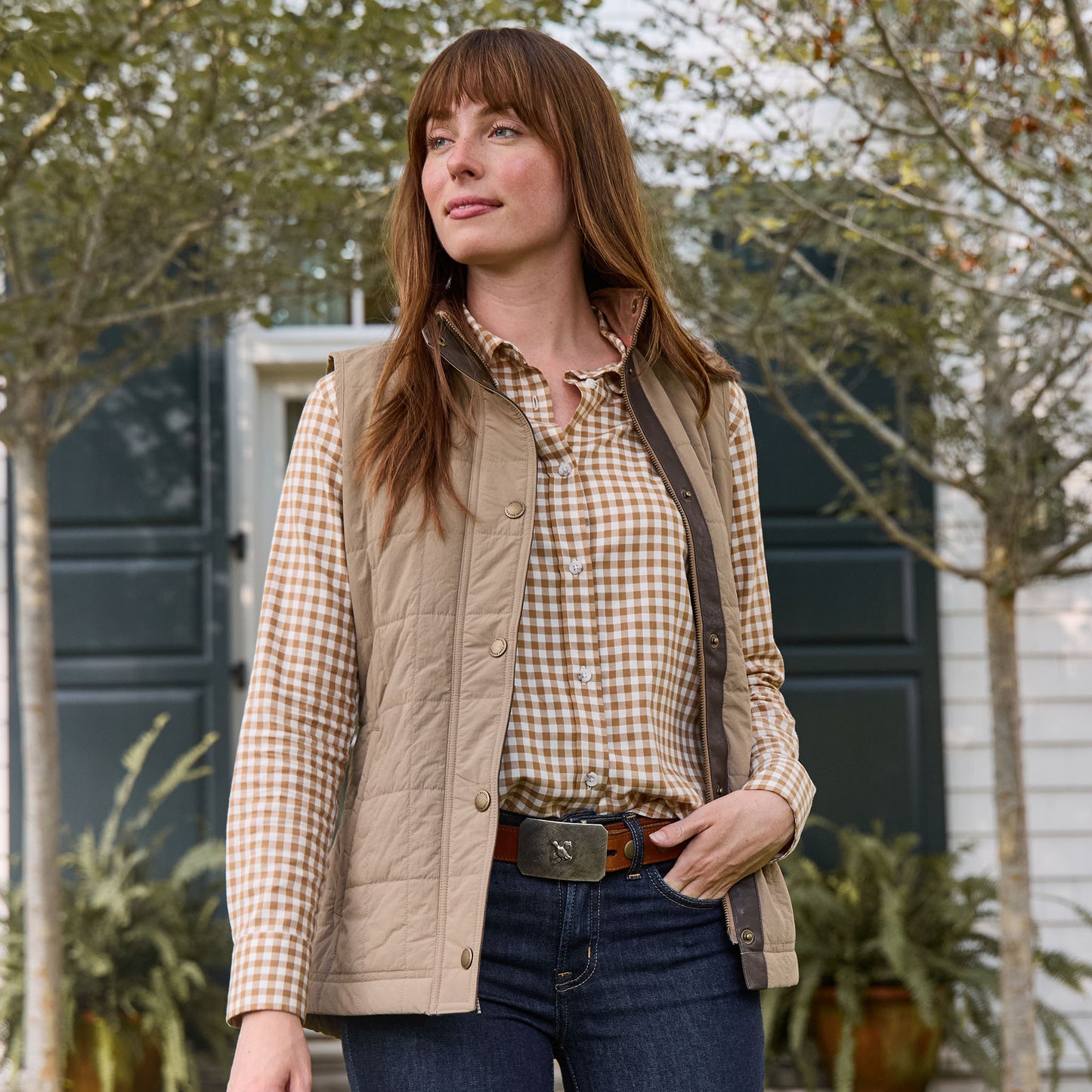 Woman outdoors in a tan vest and plaid shirt showcases the Tom Beckbe Crosshatch Quail Sterling Silver Belt Buckle.