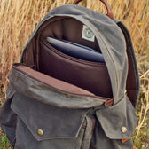 Tom Beckbe Canvas Backpack, rugged waxed design, brown and green tones, open with laptop sleeve on grass.