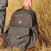A person carries a Tom Beckbe Canvas Backpack with a laptop sleeve in a grassy field.