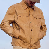 Someone in a Tom Beckbe Chatom Jacket and cap stands with hands in pockets against a clear sky.