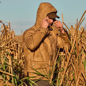 Person in a Tom Beckbe Fowler Jacket and cap, standing in a dry grassy field, adjusting their hood.