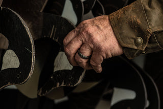 A close-up of a person’s hand with a black ring, touching stacked black and white wooden cutouts shaped like birds.