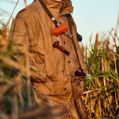 Person in a field wearing a Tom Beckbe Tensaw Jacket crafted from waxed canvas with a whistle and lanyard.