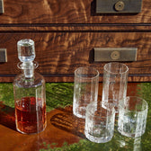 The Terrane No. 12 Decanter by Tom Beckbe: Handcrafted glassware with amber liquid and four glasses on a green-brown surface.