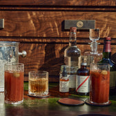 Terrane No. 12 Decanter by Tom Beckbe, liquor bottles & cocktail glasses on wood surface with ice in a metal bucket.
