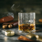 A Terrane No. 12 Glass by Tom Beckbe holds whiskey with cigars in the background.