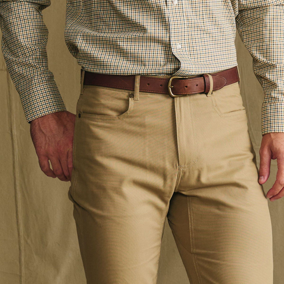 Man in tan pants and checked shirt wears a Tom Beckbe Leather Belt, standing against a neutral backdrop.