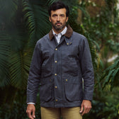 Man in Tom Beckbe Baldwin Jacket with brown collar and tan pants, outdoors by green foliage.