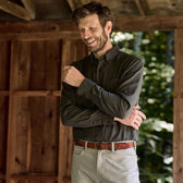 Man outdoors, smiling with eyes closed, in a Tom Beckbe Dixon Brushed Cotton Twill Shirt and light pants by wood.
