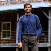 Man wearing a Tom Beckbe Dixon Brushed Cotton Twill Shirt and khaki pants stands outside a rustic wooden building.