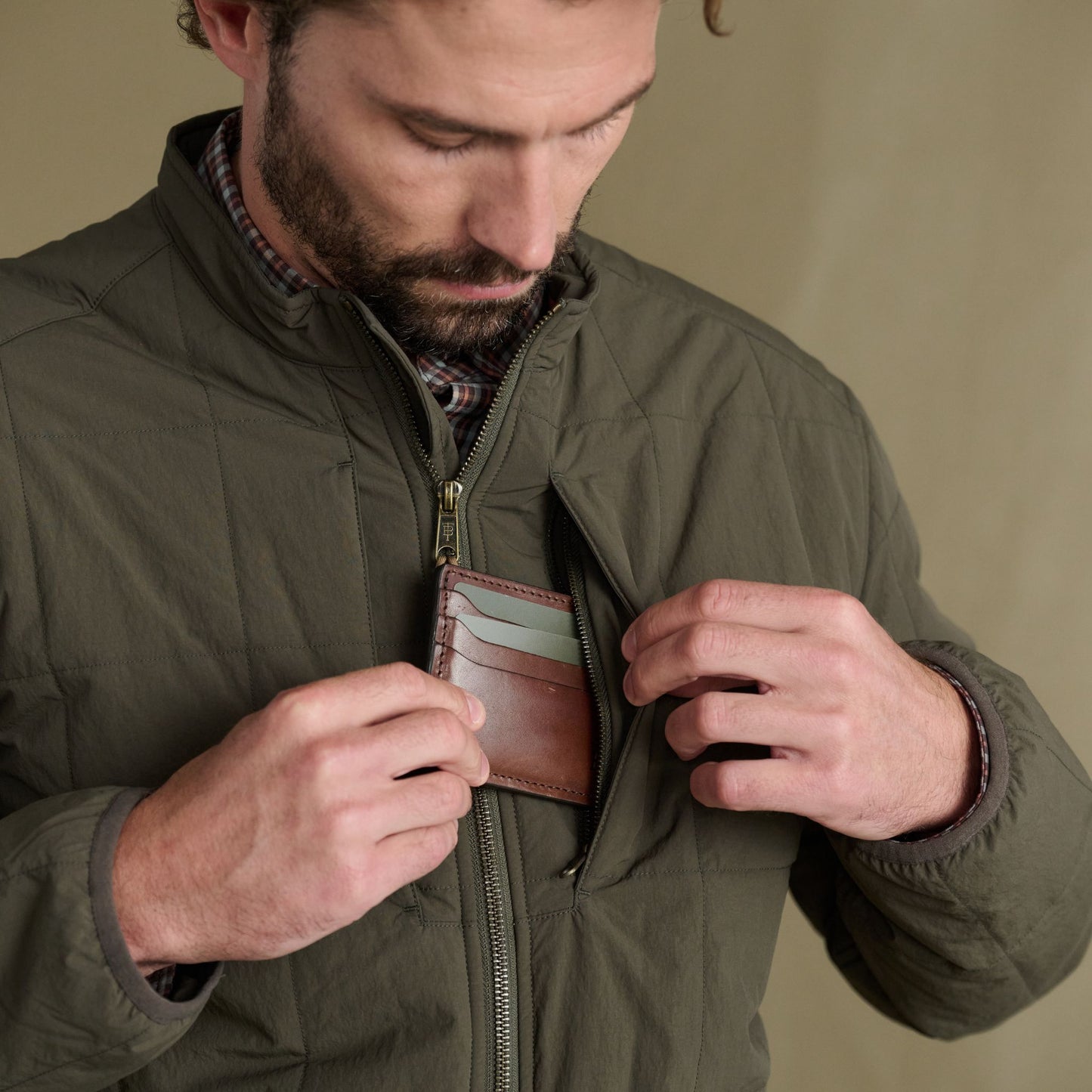 Man placing a brown leather wallet into the chest pocket of his Tom Beckbe Burgess Quilted Jacket.