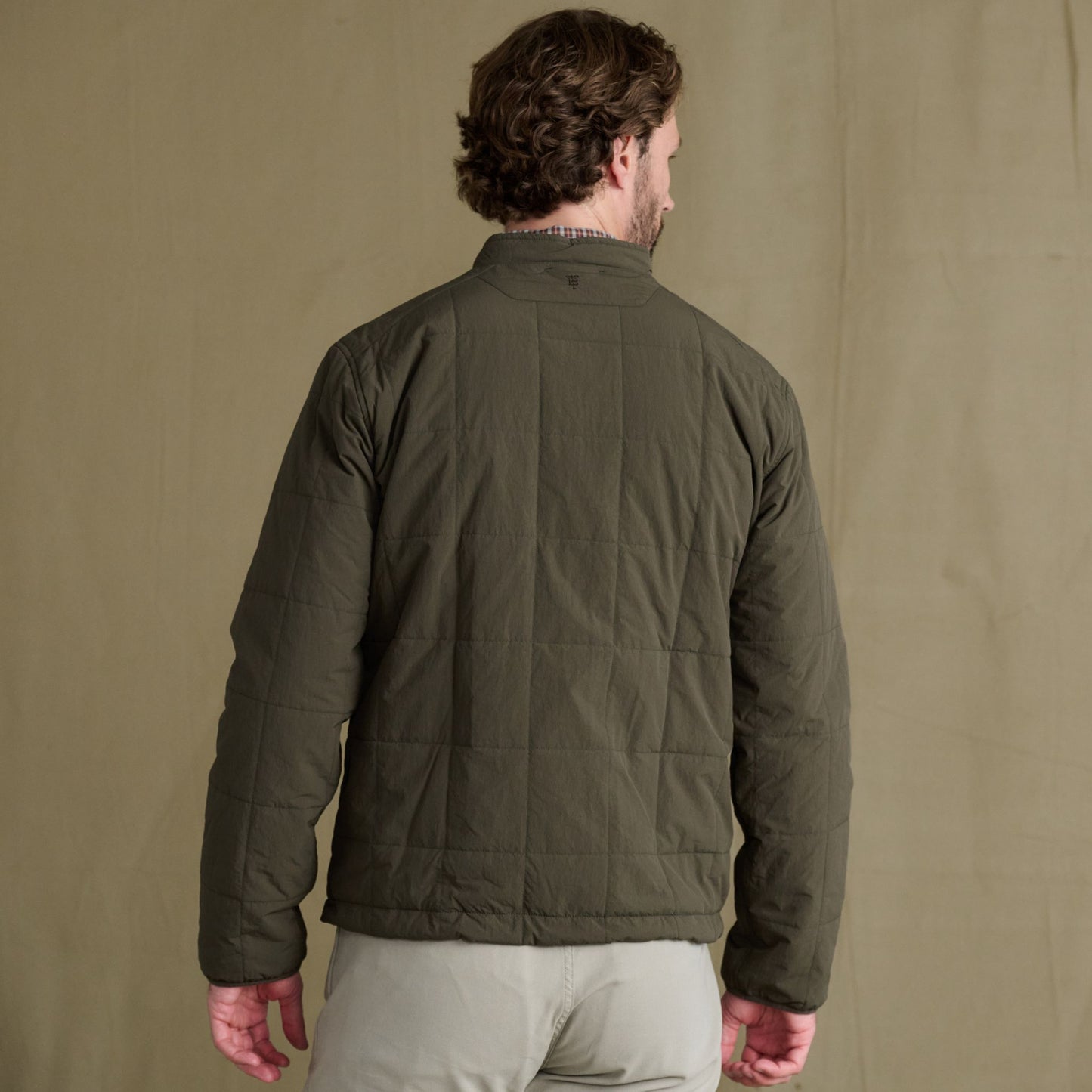 Man stands with his back to the camera in a Tom Beckbe Burgess Quilted Jacket—classic comfort, modern style.