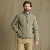 A bearded man wears the Tom Beckbe Burgess Quilted Jacket with khaki pants, standing before a beige background.