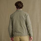 A person faces away, wearing the Tom Beckbe Burgess Quilted Jacket with khaki pants against a beige background.