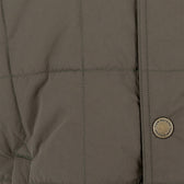 Close-up of the Tom Beckbe Burgess Quilted Vest in khaki, with visible stitching and a branded round metallic button.
