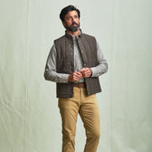 Man wearing the Tom Beckbe Burgess Quilted Vest, plaid shirt, and khaki pants against a plain light background.