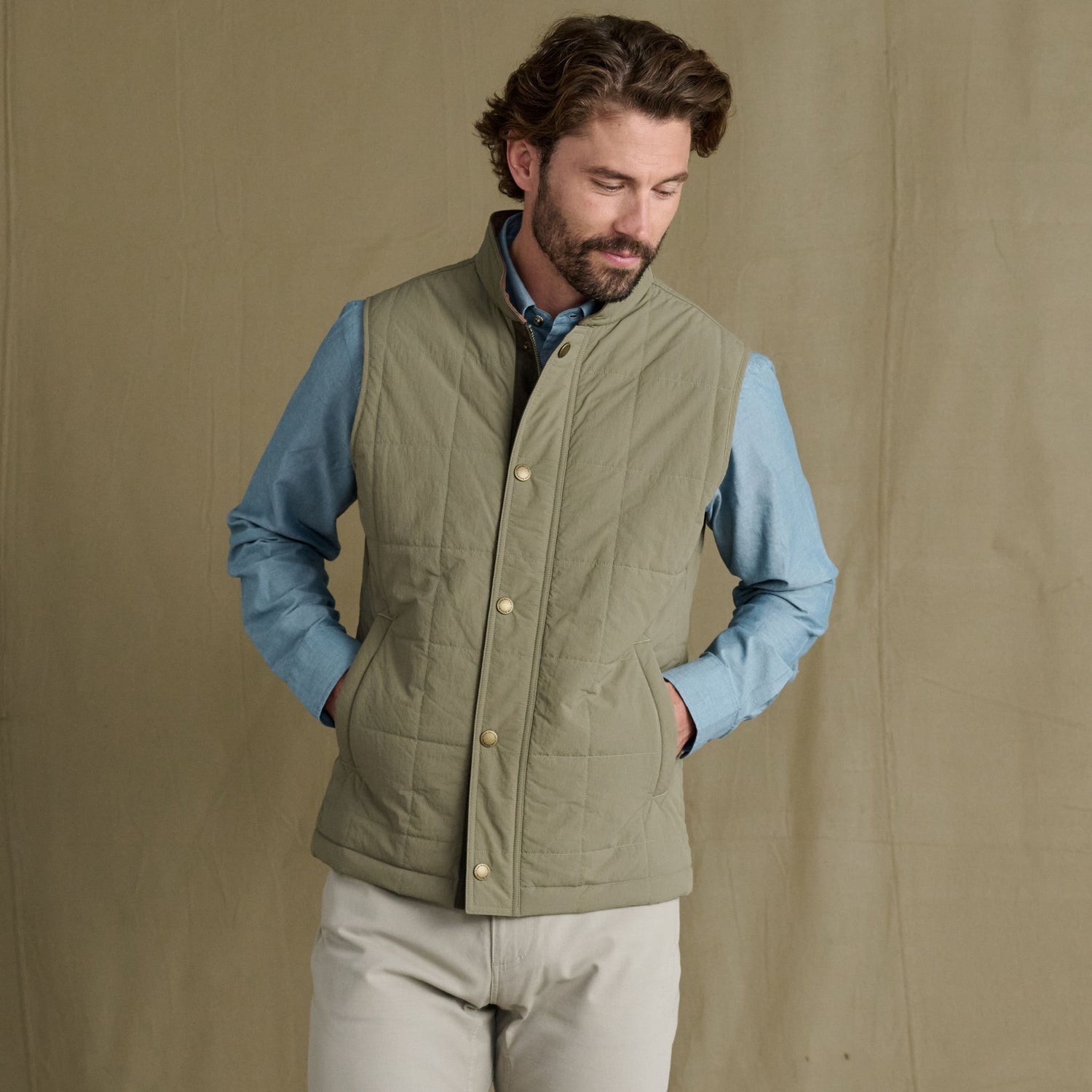 Man in Tom Beckbe Burgess Quilted Vest, light green, over blue shirt and beige pants, hands in pockets.