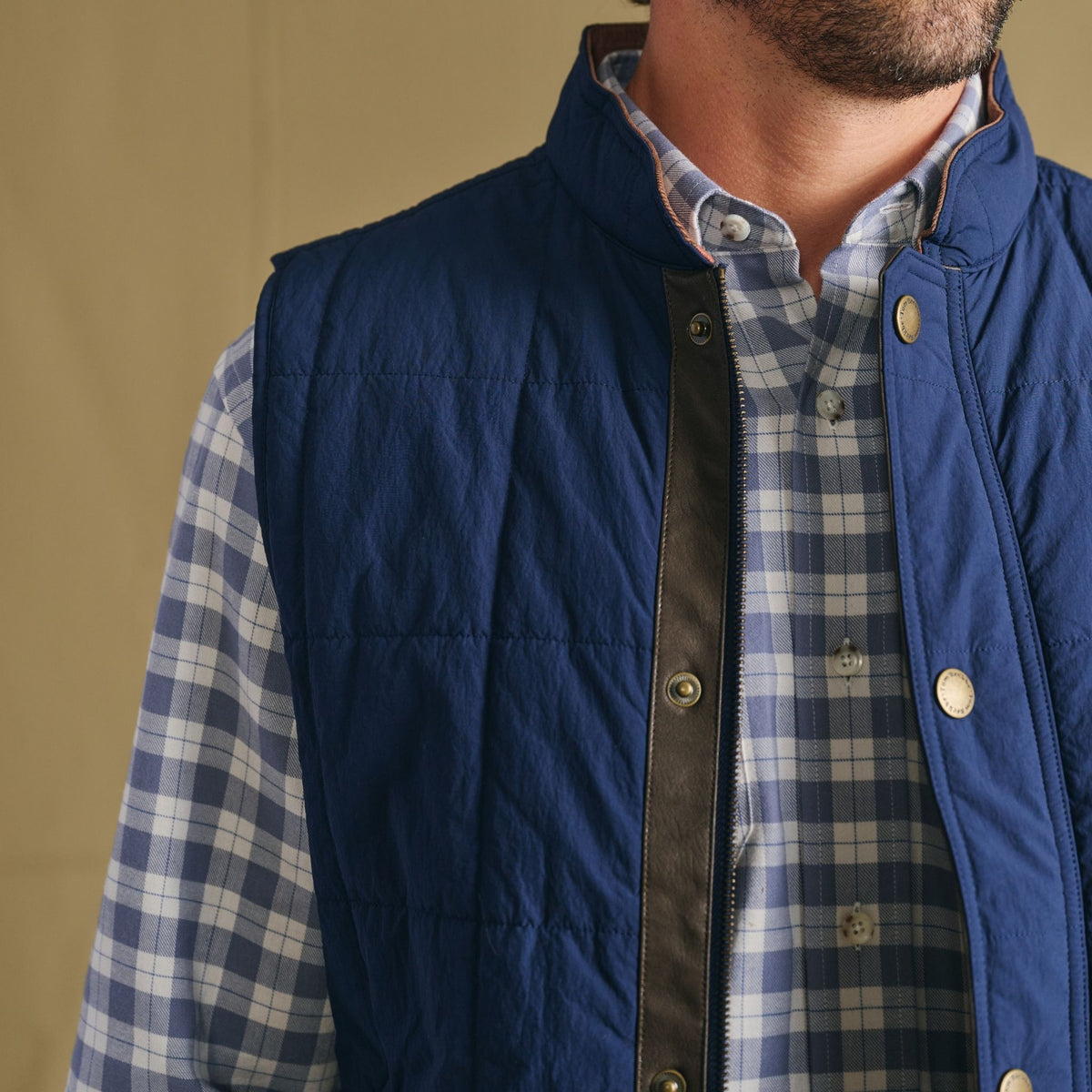 Man wears Tom Beckbe Burgess Quilted Vest over blue and white plaid shirt, shown shoulders to mid-torso.