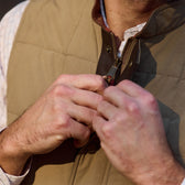 A person zipping up the Tom Beckbe Burgess Quilted Vest over a collared shirt.