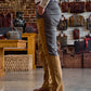A person in Tom Beckbe's Burwell Brush Pant stands indoors near wooden furniture, with bags displayed on the wall.