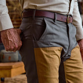 A person in Tom Beckbe Burwell Brush Pants and a brown belt stands indoors with one hand in their pocket.